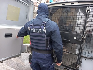 umundurowany policjantem przy klatce oznakowanego radiowozu