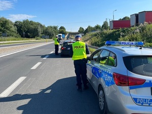 2 umundurowanych policjantów ruchu drogowego na drodze kontroluje kierującego samochodem osobowym