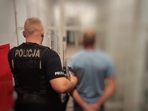 mężczyzna w kajdankach prowadzony przez umundurowanego policjanta