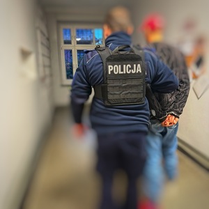 zatrzymany mężczyzna prowadzony przez policjanta w kajdankach
