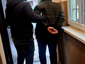 policjant po cywilnemu prowadzi do drzwi mężczyznę w kajdankach