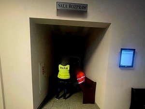 zatrzymany siedzi w sądzie przy nim umundurowany policjant