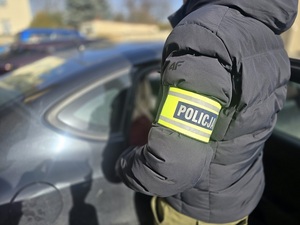 policjant nieumundurowany w opasce z napisem policja przy radiowozie