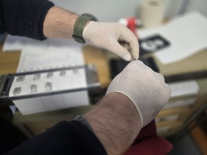 daktyloskopowanie, widzimy jak mężczyzna w białych rękawiczkach pobiera odciski palców