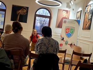 osoby siedzące tyłem, przed nimi kobieta klęczy przy fantomie