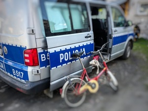 rower i radiowóz na drodze w dzień, w tle zabudowania mieszkalne