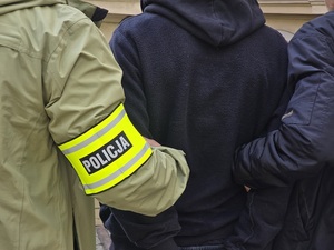 mężczyzna w kajdankach prowadzony przez nieumundurowanych policjantów