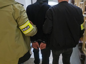 mężczyzna w kajdankach prowadzony przez nieumundurowanych policjantów